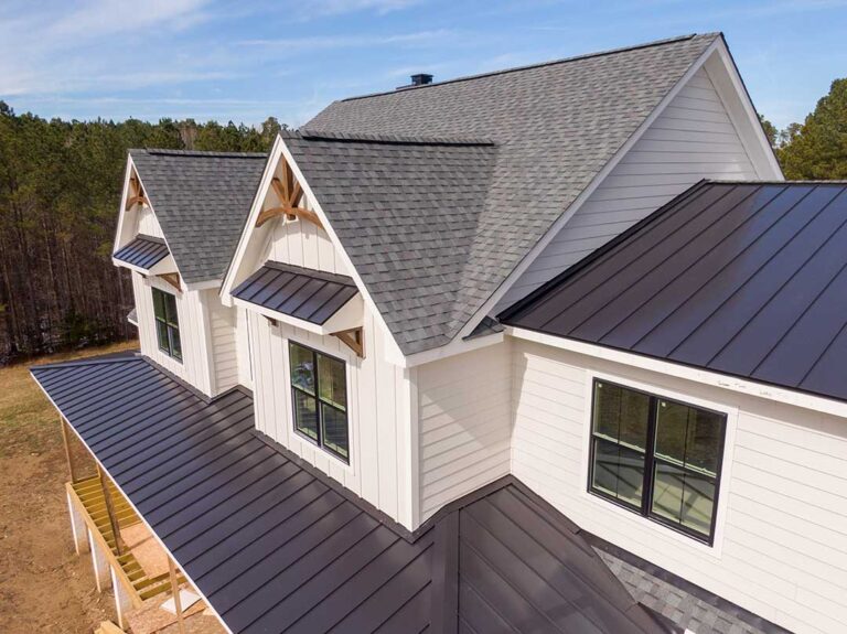 A homeowner using a roof rake with an extension pole to remove leaves from a pitched shingle roof.