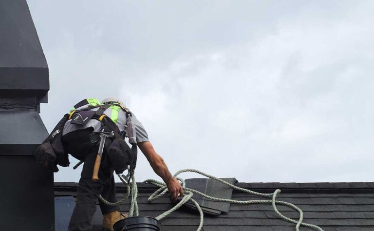 Hand pointing at a round shingle mark and scattered granules on a residential roof after a recent storm.